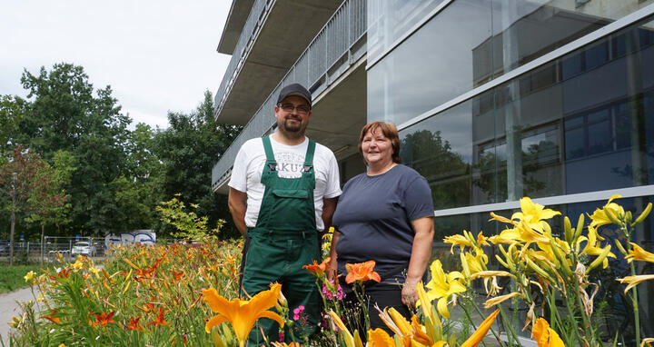 Ein Mann und eine Frau stehen in einer Grünanlage vor einem Gebäude