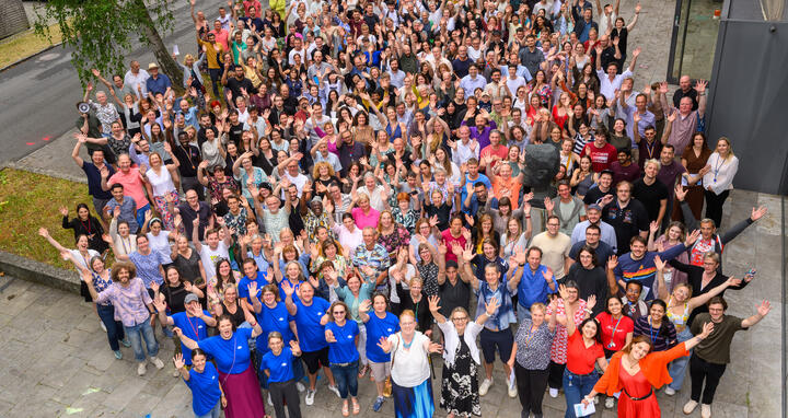 Large group photo of attendees waving at Summer Science Day 2025 outside a research facility.