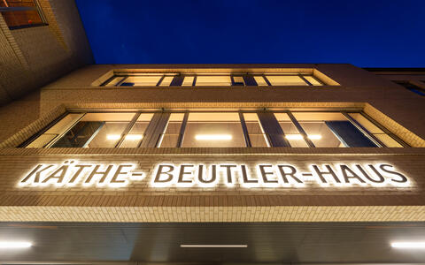 Tür zum Foyer des Käthe-Beutler-Hauses (EG) mit Blick zur Hausfassade und den Seminarräumen (1. und 2. OG) bei Dämmerung