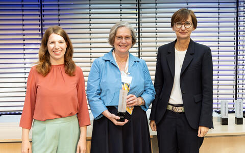 3 Frauen auf der Bühne, eine hält eine Trophäe in der Hand.