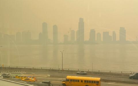 Blick aus einem Fenster: Im Hintergrund die Skyline von New York im Nebel; im Vordergrund Straße, wo Autos u.a. ein amerikanischer Schulbus fahren.