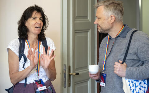 Two conference participants having a casual conversation during a break, one holding a coffee cup.