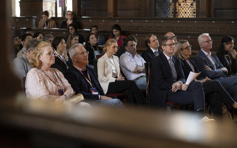 Audience members in formal attire attentively listening during a lecture or conference session.