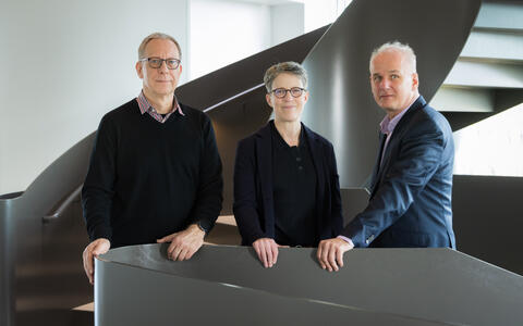 Three people pose together on a modern staircase.