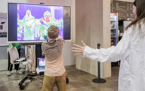 Child interacts with thermal imaging screen during a science demonstration.
