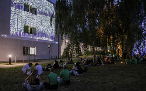 People watch abstract visuals projected on a building at night.