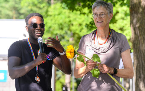 Man speaking into a microphone beside a woman holding a sunflower on stage.