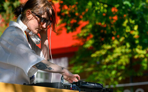 DJ performing outdoors with headphones and mixer at a daytime event.