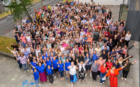 Large group photo of attendees waving at Summer Science Day 2025 outside a research facility.