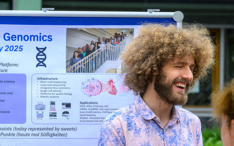 Man smiling in front of a genomics research poster at a science event.