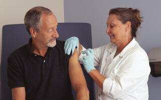 Healthcare worker administering a vaccine to an older man in a clinical setting.