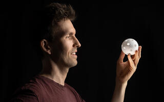 Lachender Mann hält eine weiße, gelochte 3D-gedruckte Kugel in der Hand.