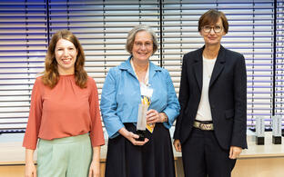 3 Frauen auf der Bühne, eine hält eine Trophäe in der Hand.