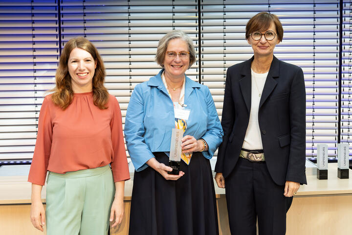 3 Frauen auf der Bühne, eine hält eine Trophäe in der Hand.