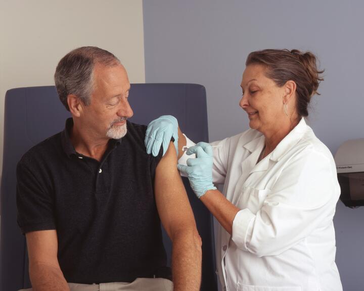 Healthcare worker administering a vaccine to an older man in a clinical setting.