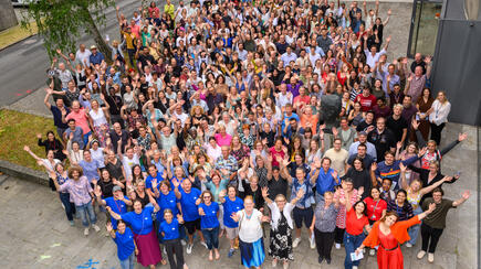 Large group photo of attendees waving at Summer Science Day 2025 outside a research facility.
